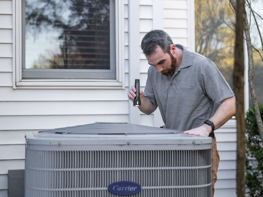 An HVAC technician servicing an outdoor air-conditioning unit